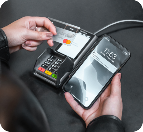Une personne paie par carte à un terminal de point de vente et reçoit simultanément une notification sur l'écran de son portable pour un ticket de caisse dématérialisé.
